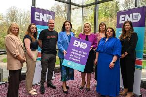 Image of eight people, two holding an Ending Violence Against Women and Girls (EVAWG) sign. The First Minister Michelle O'Neill and deputy First Minister Emma Little-Pengelly (centre) pictured with stakeholders at the launch of the second EVAWG Delivery Plan.